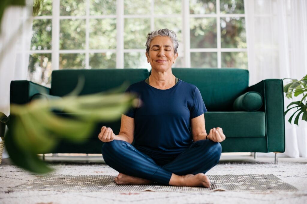 Senior,Woman,Meditating,In,Lotus,Position,At,Home,,Sitting,On